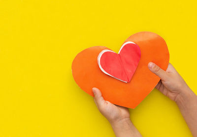 Cropped hand holding heart shape against yellow background