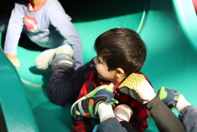 High angle view of siblings sliding on slide in playground