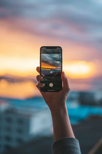 Hand holding smart phone against sea during sunset