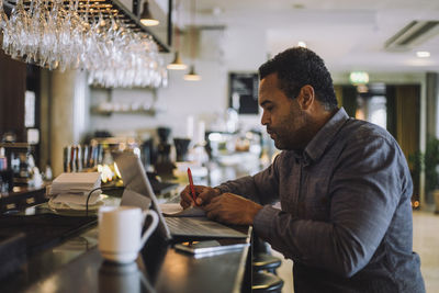 Businessman writing while sitting with laptop at bar counter