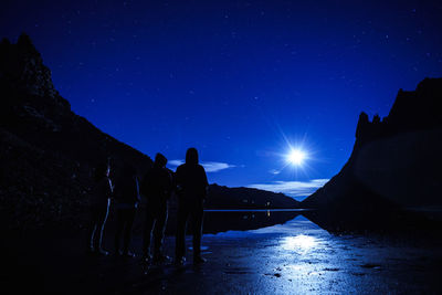 People standing by lake at night