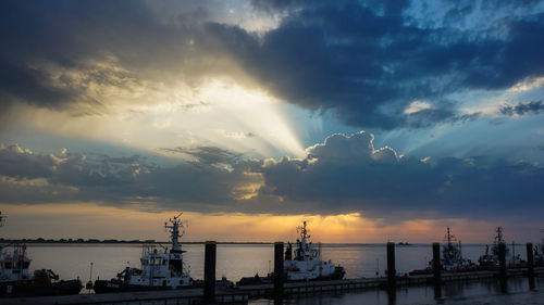 Boats moored by pier in sea against cloudy sky during sunset