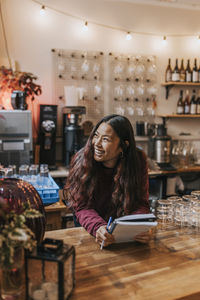 Happy young female cafe owner with diary leaning on table