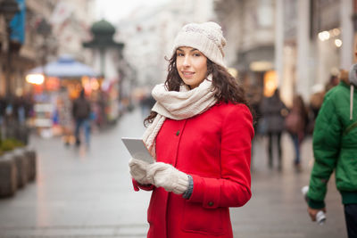 Portrait of young woman using smart phone while standing on city street
