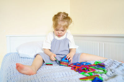 Curious little girl playing with magnetic construction toy while sitting on bed