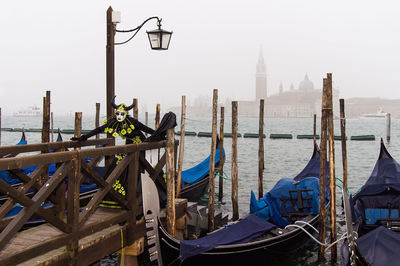 Venetian carnival and boats moored in sea against sky