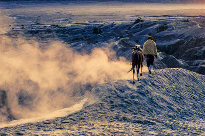 Rear view of mid adult man with horse walking on mountain during sunset