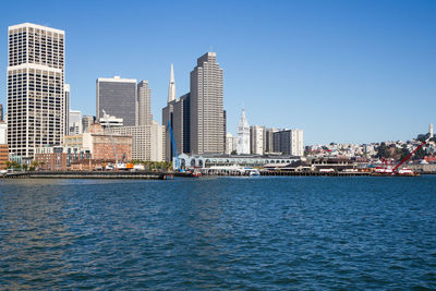 Sea by cityscape against clear blue sky