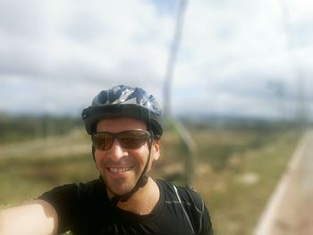 Portrait of happy cyclist standing on field against sky