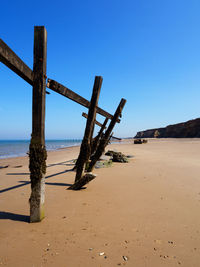 Wooden post on beach against clear blue sky