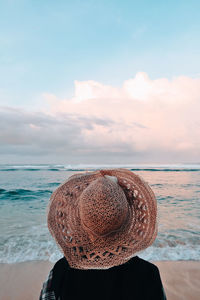 Rear view of woman wearing hat at beach against sky