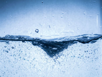 Close-up of water splashing on glass against blue background