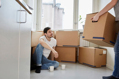 Man with coffee mugs looking at woman carrying cardboard boxes in new house