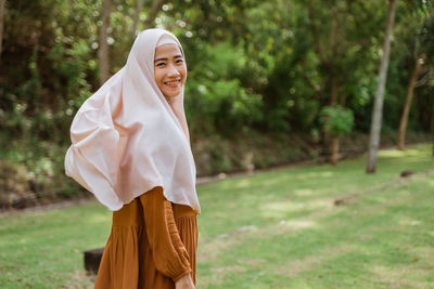 Portrait of young woman standing against trees