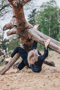 Full length of woman climbing on tree trunk in forest