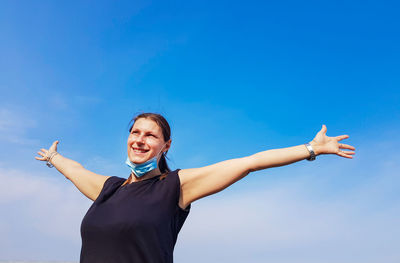 Happy woman with arms outstretched standing against blue sky