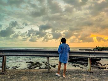 Rear view of girl looking at sea against sunset sky