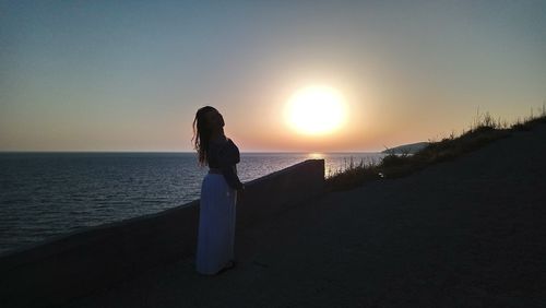 Woman looking at sea against sunset sky