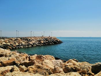 Rocks by sea against clear blue sky