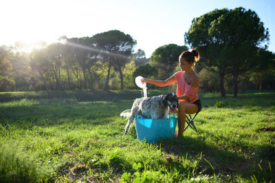 Middle-aged woman bathing her dog in the garden on a sunny day surrounded by trees.