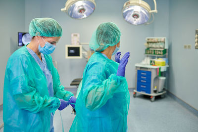 Side view of unrecognizable medic helping female coworker tying sterile uniform in hospital