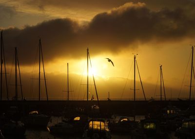 Sailboats moored on sea against dramatic sky during sunset