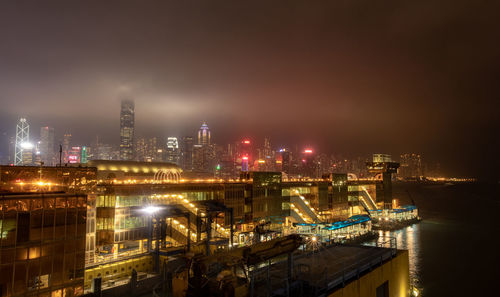 Illuminated buildings by river against sky at night