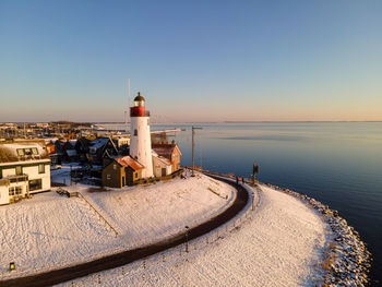 Lighthouse by sea against buildings against clear sky