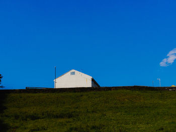 Barn on field against clear blue sky