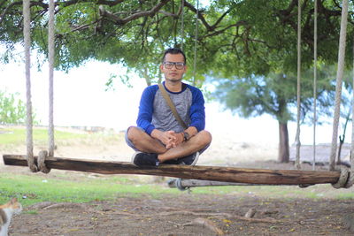 Portrait of young man sitting on plant against trees