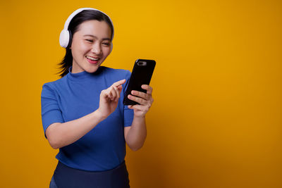 Smiling young woman using mobile phone against yellow background