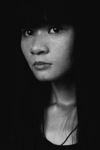 Close-up of thoughtful young woman with bangs looking away against black background