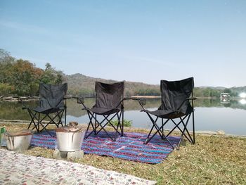 Chairs and table by lake against sky
