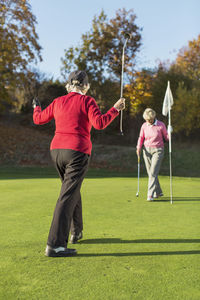 Full length rear view of senior female golfer playing with friend on golf course