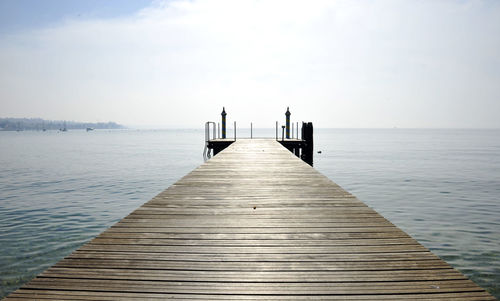 Wooden jetty leading to pier over sea against sky