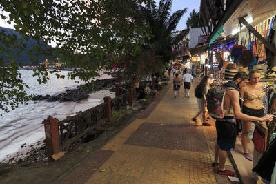 People walking on sidewalk in city against sky