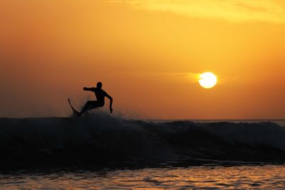 Silhouette man surfing in sea against sky during sunset