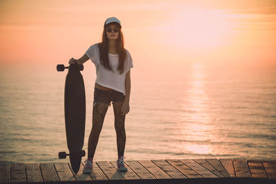 Woman standing by sea against sky during sunset