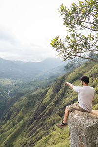 Man sitting on mountain against sky