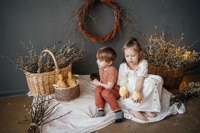 Brother and sister with small goslings in a wicker basket eco style gray willow background