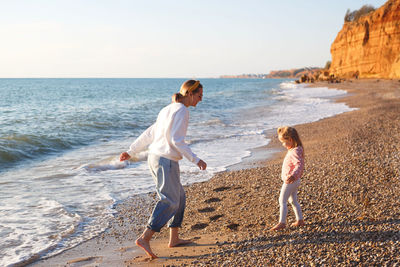 Mother and daughter at beach against sea and sky