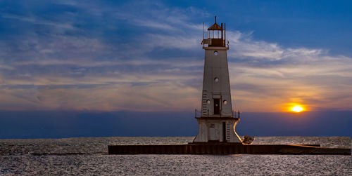 Lighthouse by sea against sky during sunset