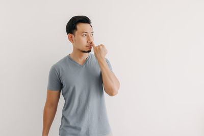 Young man looking away while standing against white background