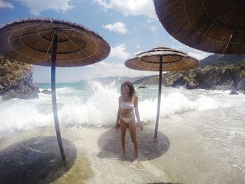 Young woman standing amidst parasols with waves reaching on shore