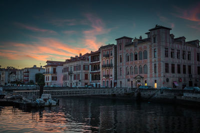 Buildings by canal against sky at sunset