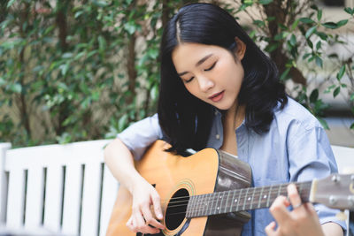 Young woman playing guitar while sitting in park