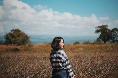 Young woman standing on field against sky