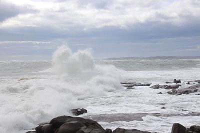 Waves splashing on rocks at shore against sky