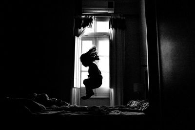 Side view of silhouette girl jumping on bed in darkroom at home