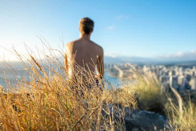 Close-up of grass against shirtless man looking at view from mountain
